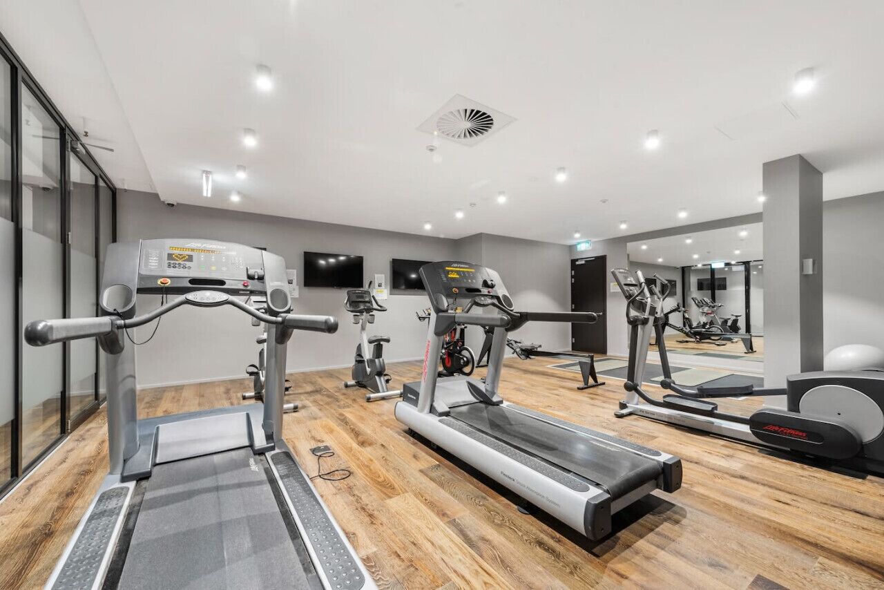 Een moderne sportschool met cardioapparatuur, een spiegel en een houten vloer.
