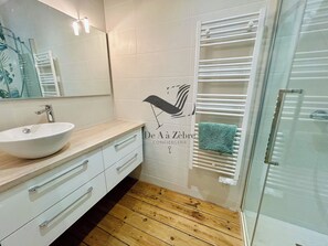 A modern bathroom with a white sink, wooden vanity, a glass shower enclosure, and a towel rack with a green towel. - Le Gambetta - Close to downtown & the thermal baths (Rochefort)