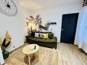 A living room with a green sofa, a round coffee table, a wall-mounted lamp, and a decorative wall piece. - Le Gambetta - Close to downtown & the thermal baths (Rochefort)