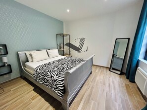 A modern bedroom with a bed, a bedside table, a mirror, and a geometric-patterned wall. - Le Gambetta - Close to downtown & the thermal baths (Rochefort)