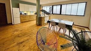 Une cuisine moderne avec des meubles en bois, un coin repas comprenant une table et des chaises, et une grande fenêtre avec des stores.