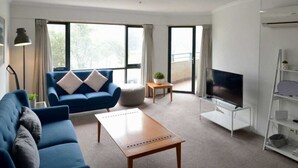 A modern living room with a blue sofa, a wooden coffee table, a flat-screen TV, and a white entertainment unit.