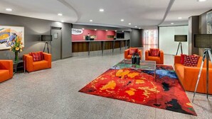 A modern lobby with orange seating, a reception desk, and a colorful carpet.