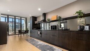 Una cocina moderna con armarios oscuros, un ventanal grande y una zona de comedor con sillas.