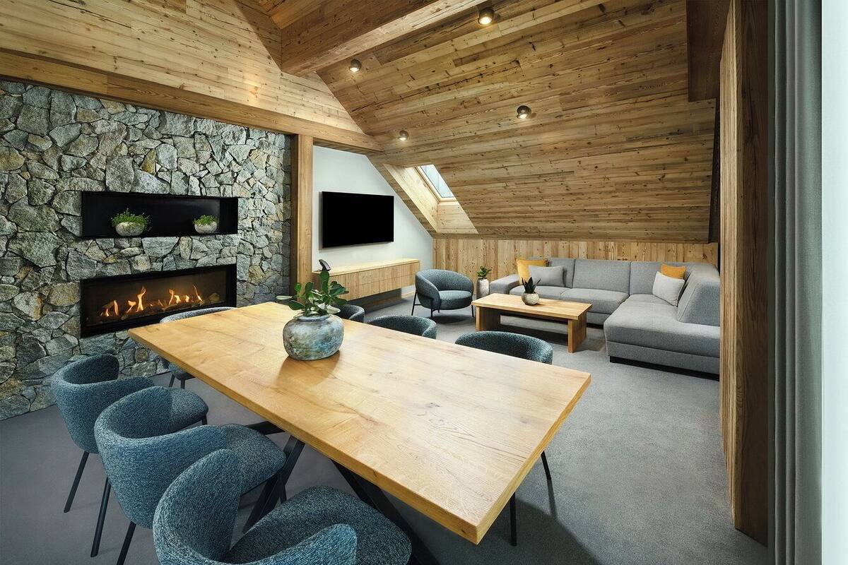 Una sala de estar acogedora con pared de piedra, techo de madera y chimenea. Hay un sofá, una mesa de centro y un televisor montado en la pared.