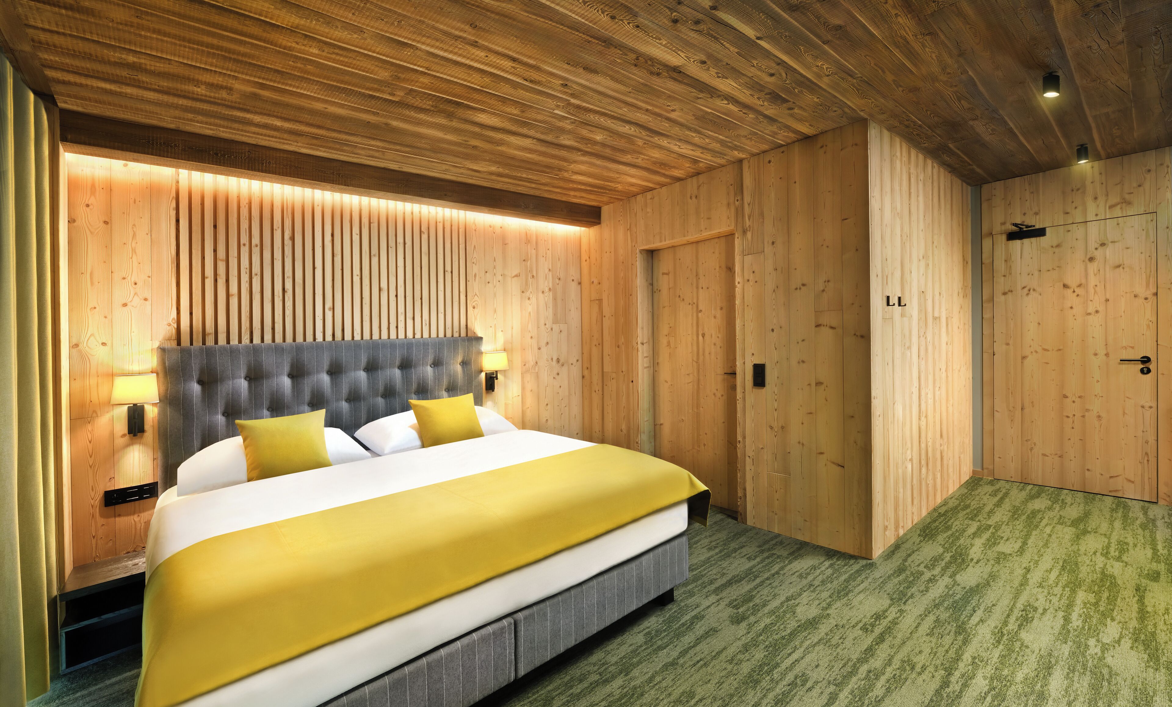 A bedroom with a bed, wooden walls, and a green carpet.