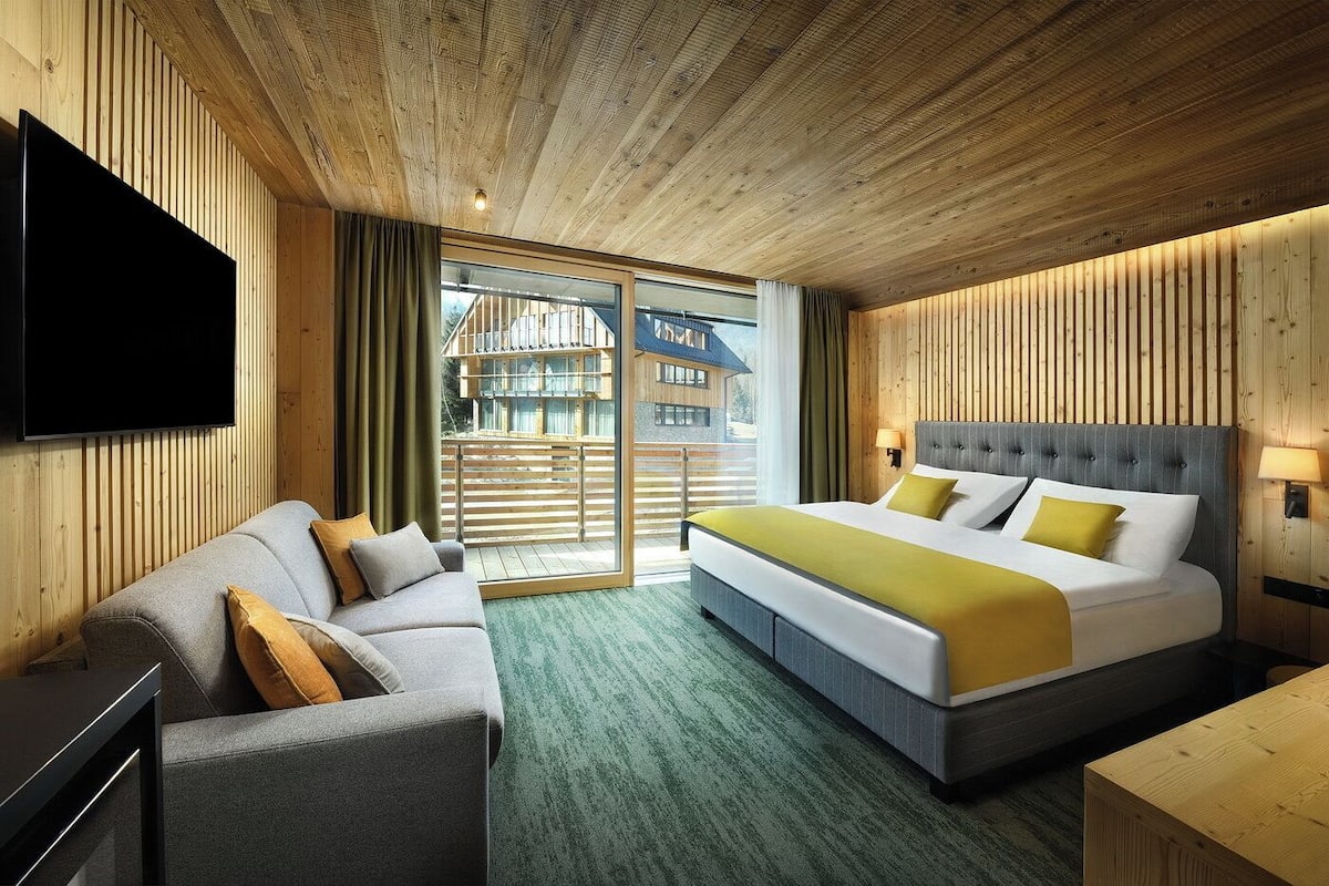 Una habitación de hotel con cama, sofá, televisión y balcón con barandilla de madera.