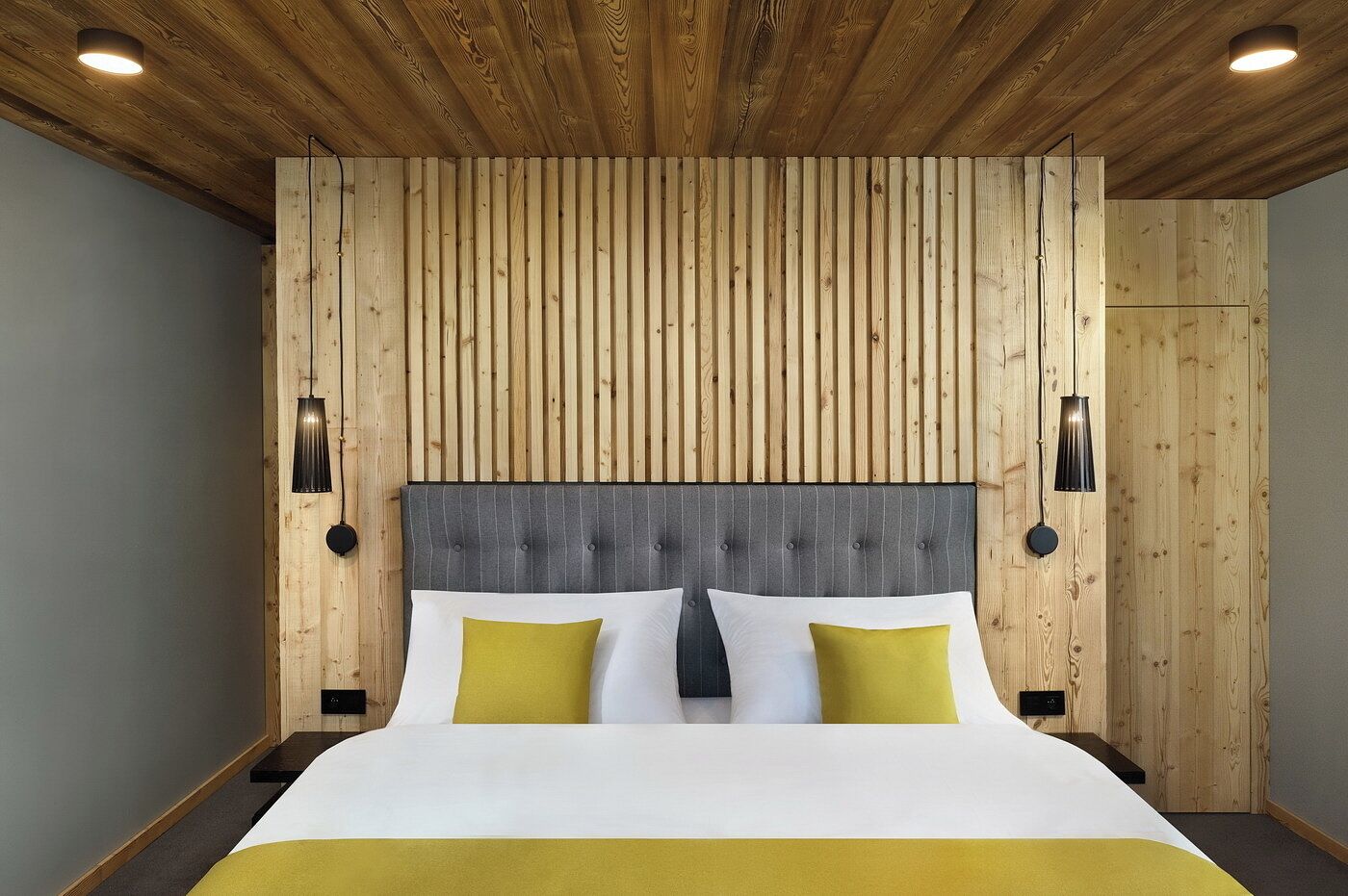 A bedroom with a wooden slat wall, a tufted headboard, and two bedside lamps.