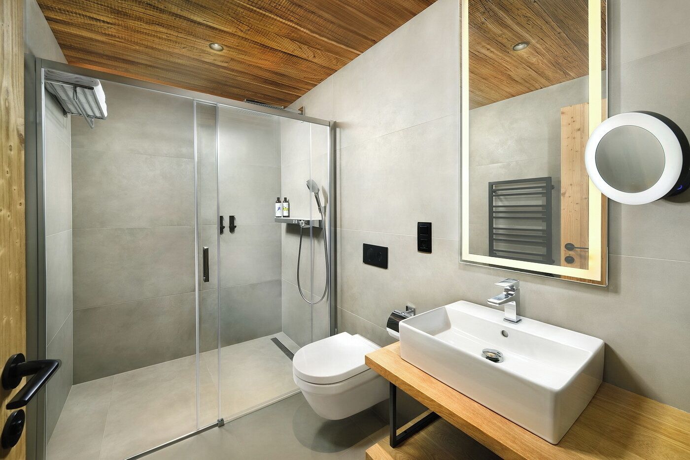 A modern bathroom with a glass-enclosed shower, a white sink, and a wooden vanity.