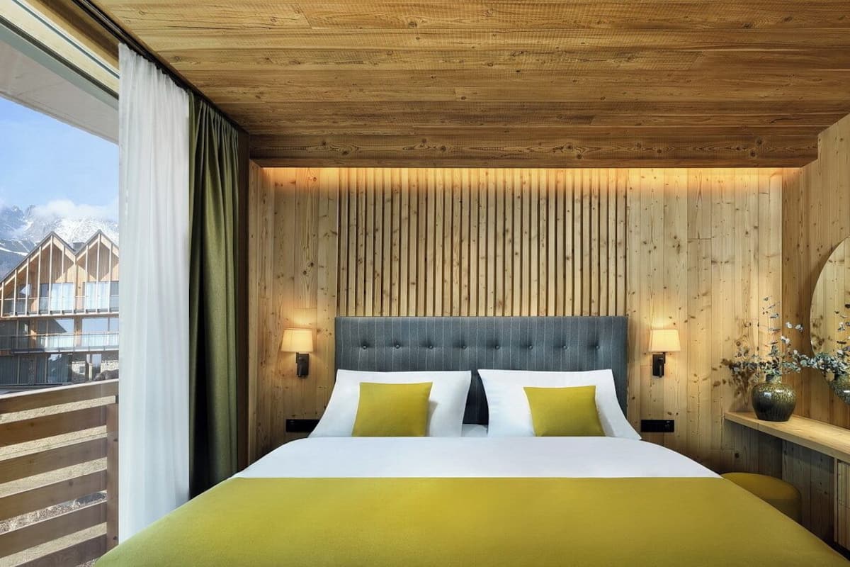 Habitación de hotel con una cama grande, paneles de madera, vistas a las montañas y un balcón.