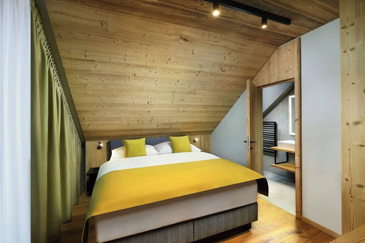 Un dormitorio con techo de madera, cama con colcha amarilla y ventana con cortinas.