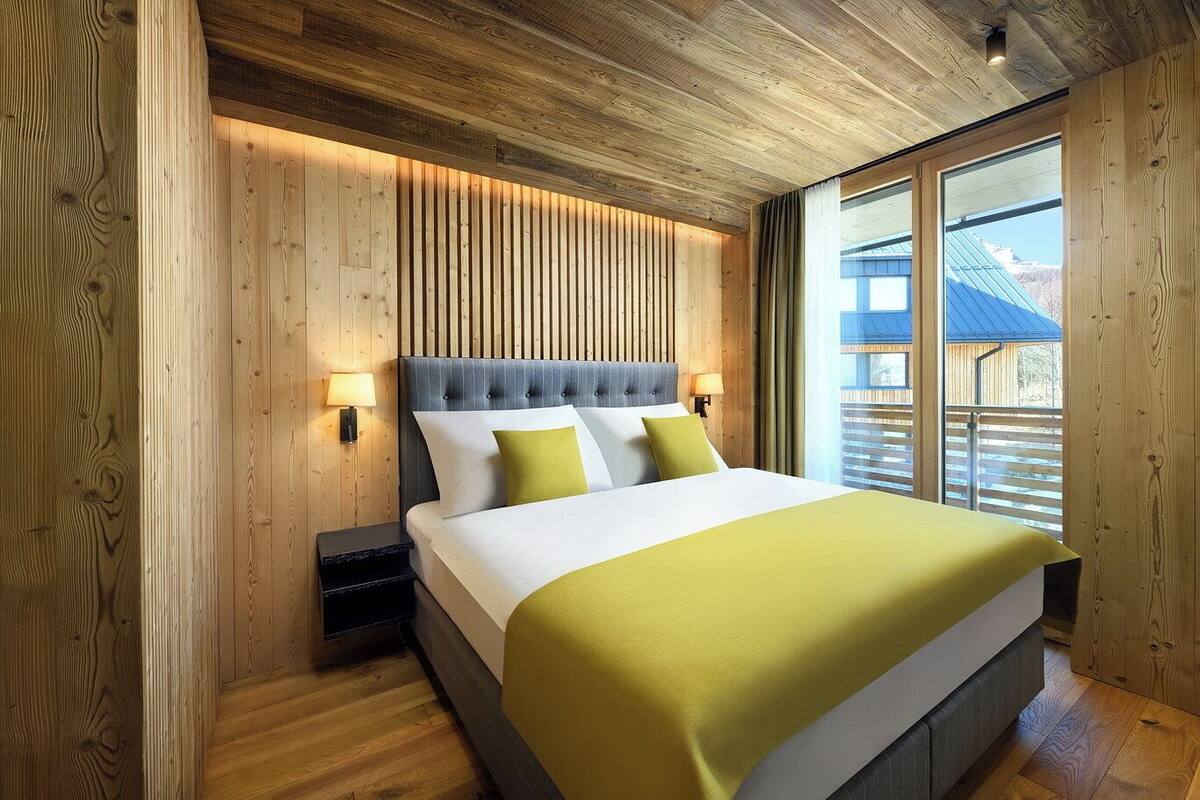 Un dormitorio con paneles de madera, una cama grande, dos lámparas de noche y vistas a un edificio con tejado azul.