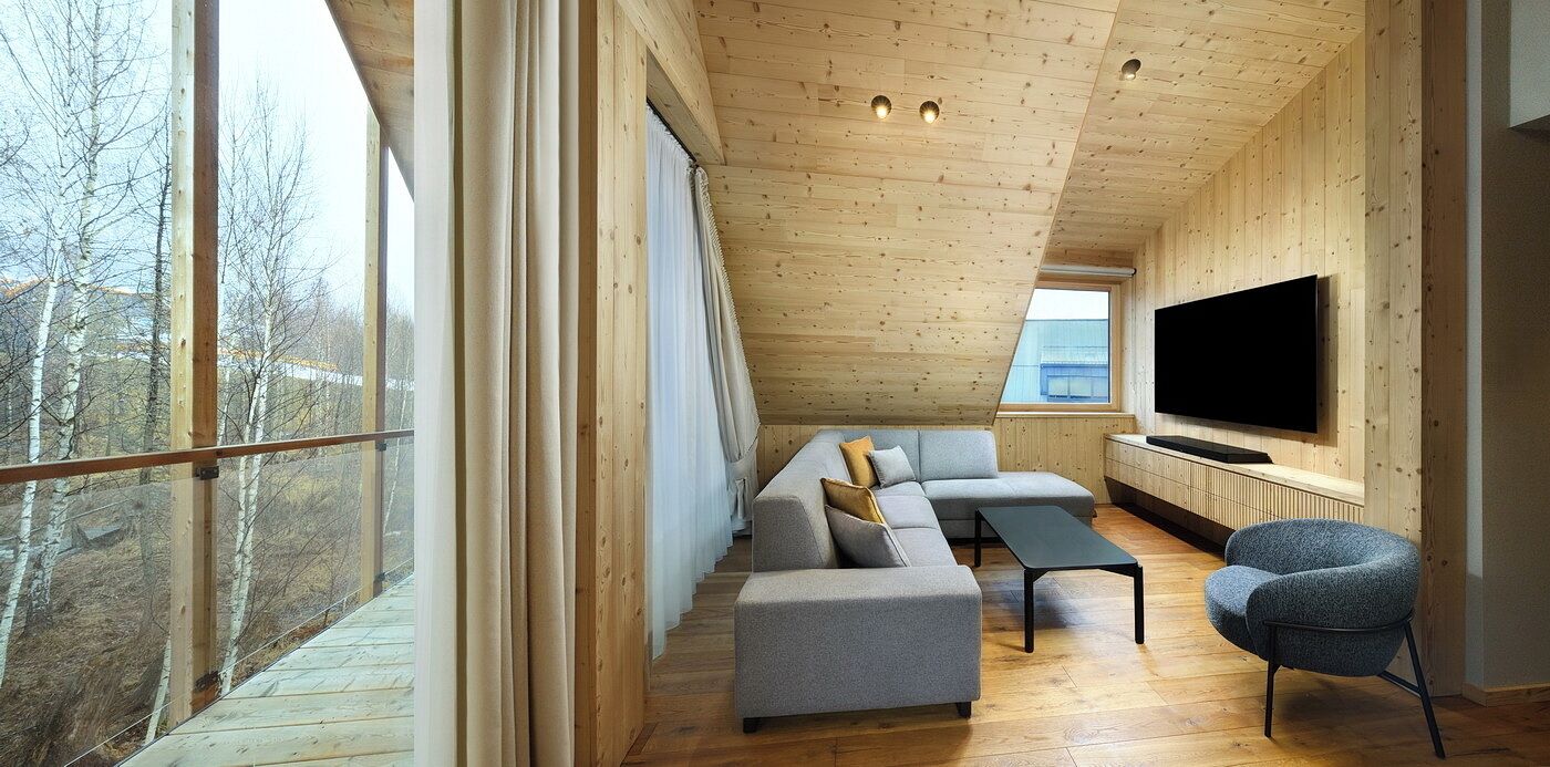 A modern living room with a large window, a flat-screen TV, a grey sofa, and a blue armchair.