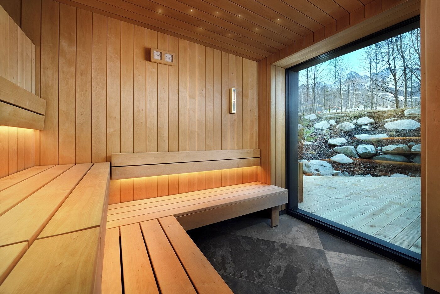Un sauna avec des bancs en bois et une porte en verre donnant sur un espace extérieur rocheux.