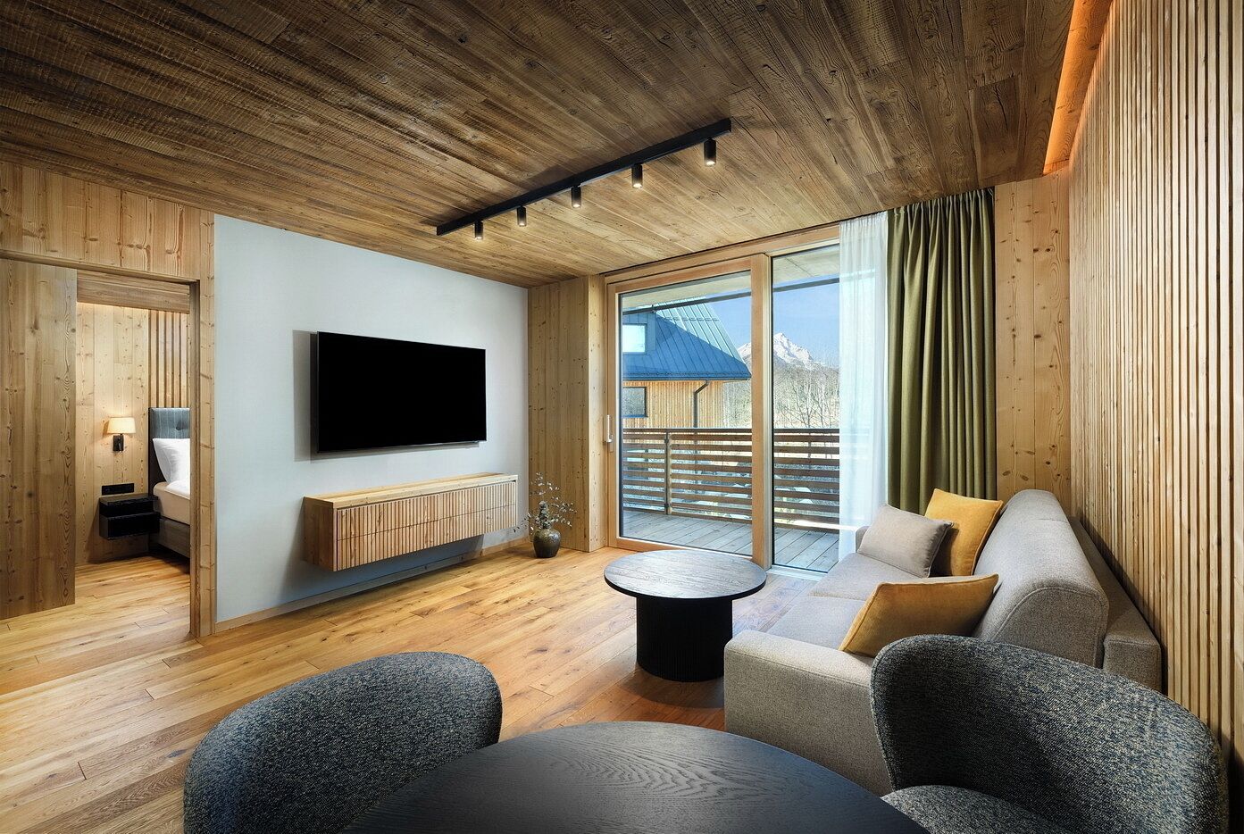 A modern interior with a wooden ceiling, a flat-screen TV mounted on the wall, a sofa, and a small round table.