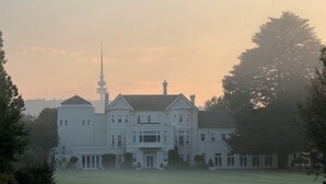 A large, multi-story building with a prominent tower, surrounded by a well-maintained lawn.