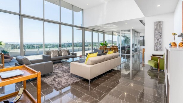 A spacious living area with large windows, a modern sofa, a glass coffee table, and a view of the city.