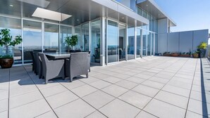 A modern outdoor patio with a glass-enclosed area, wicker furniture, and potted plants.