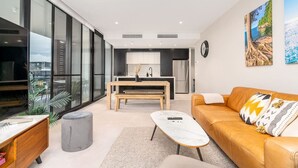 Una sala de estar moderna con un sofá, una mesa de centro y vistas a una cocina y un balcón.