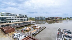 Una marina con varias embarcaciones amarradas, un edificio moderno de varios pisos y una masa de agua tranquila que refleja las estructuras.