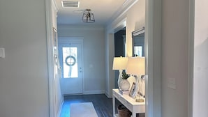 Un corridoio con pavimento in legno, una panca bianca con una lampada e una porta decorata con un'corona.