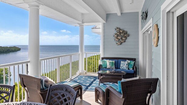 A covered porch with wicker furniture, a view of the ocean, and a decorative wall piece.