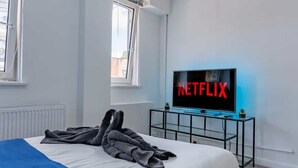 A modern bedroom with a bed, a TV displaying the Netflix logo, and a window.