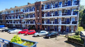 A multi-story residential building with balconies, a parking area, and a clear blue sky.