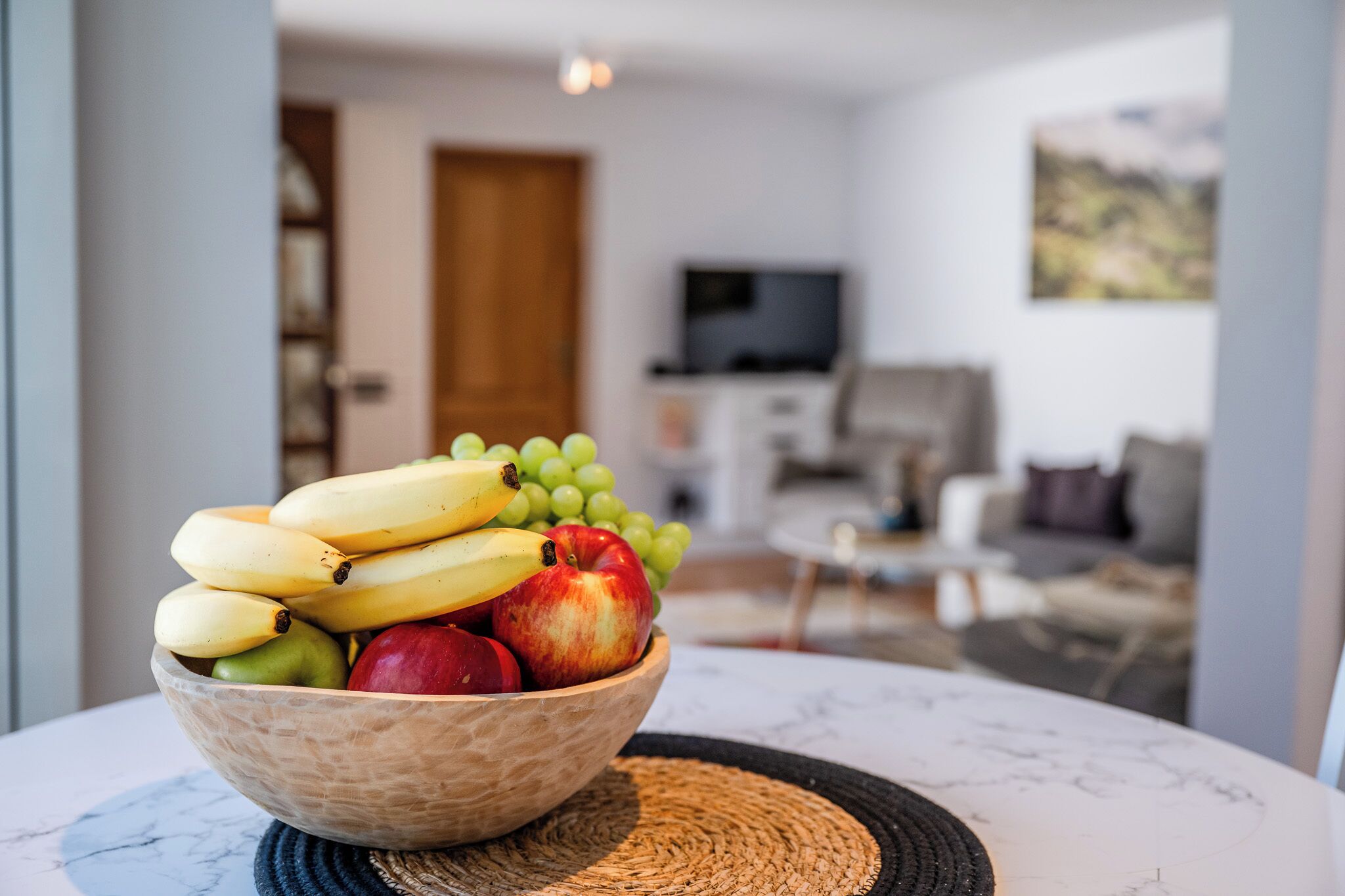 A bowl of fruit on a table in a modern living room with a TV and a painting on the wall.