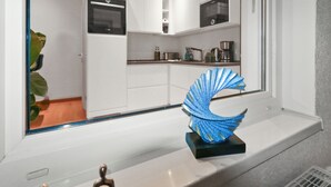 A modern kitchen with white cabinets, a built-in oven, and a window with a decorative blue sculpture.