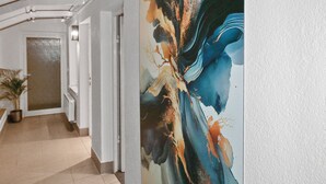 A hallway with a large abstract painting on the wall, a potted plant, and a door at the end.