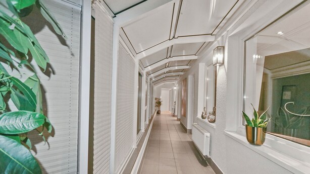 A corridor with white walls, a tiled floor, and a potted plant on the right.