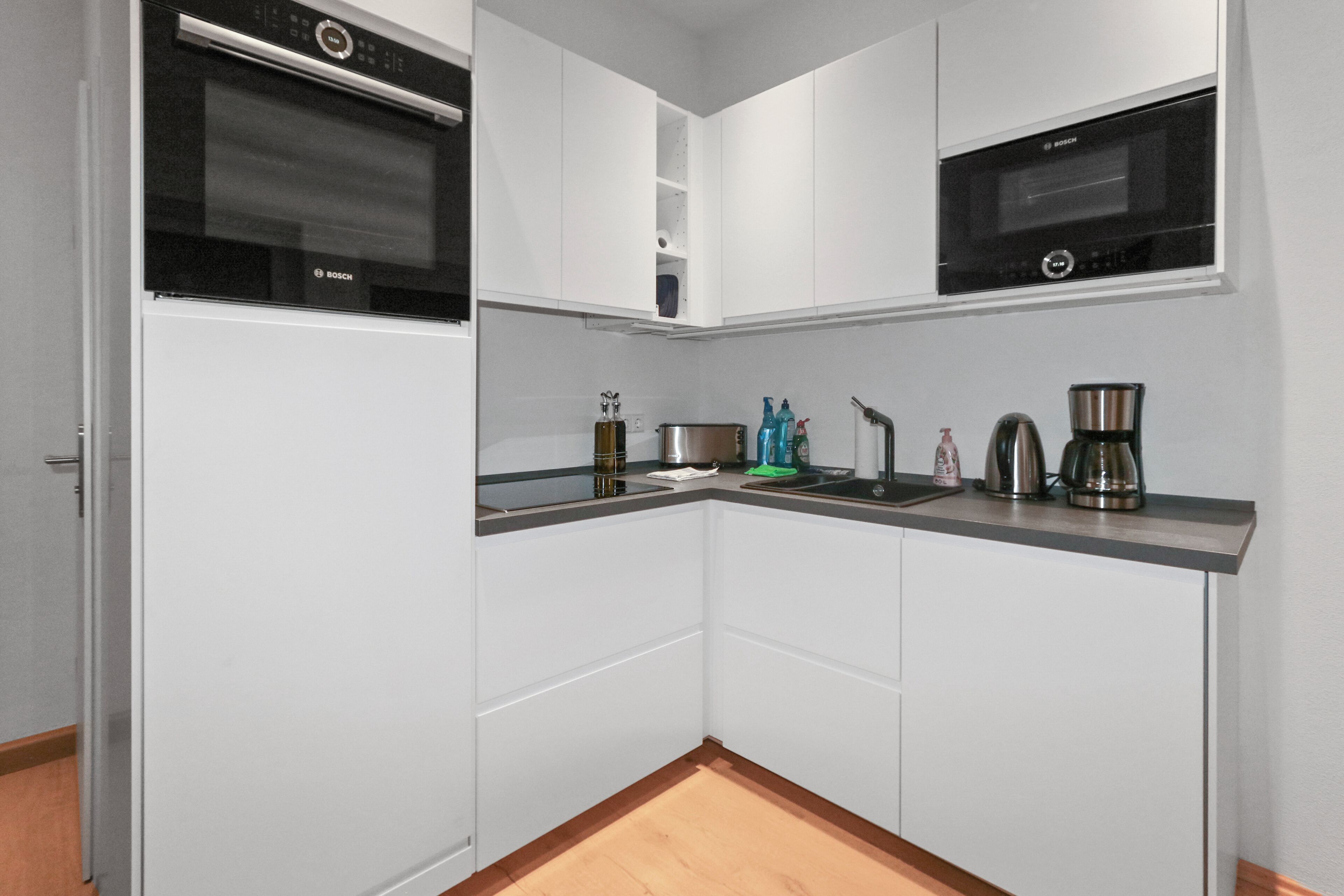 Eine moderne Küche mit weißen Schränken, einem Backofen von Bosch, einer Mikrowelle von Bosch, einer Kaffeemaschine und einem Spülbecken.