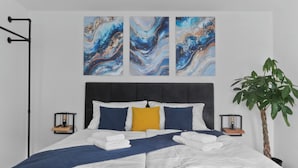 A neatly made bed with white linens, a blue throw blanket, and a yellow pillow. There are two bedside tables with lamps, a large potted plant, and abstract art on the wall.