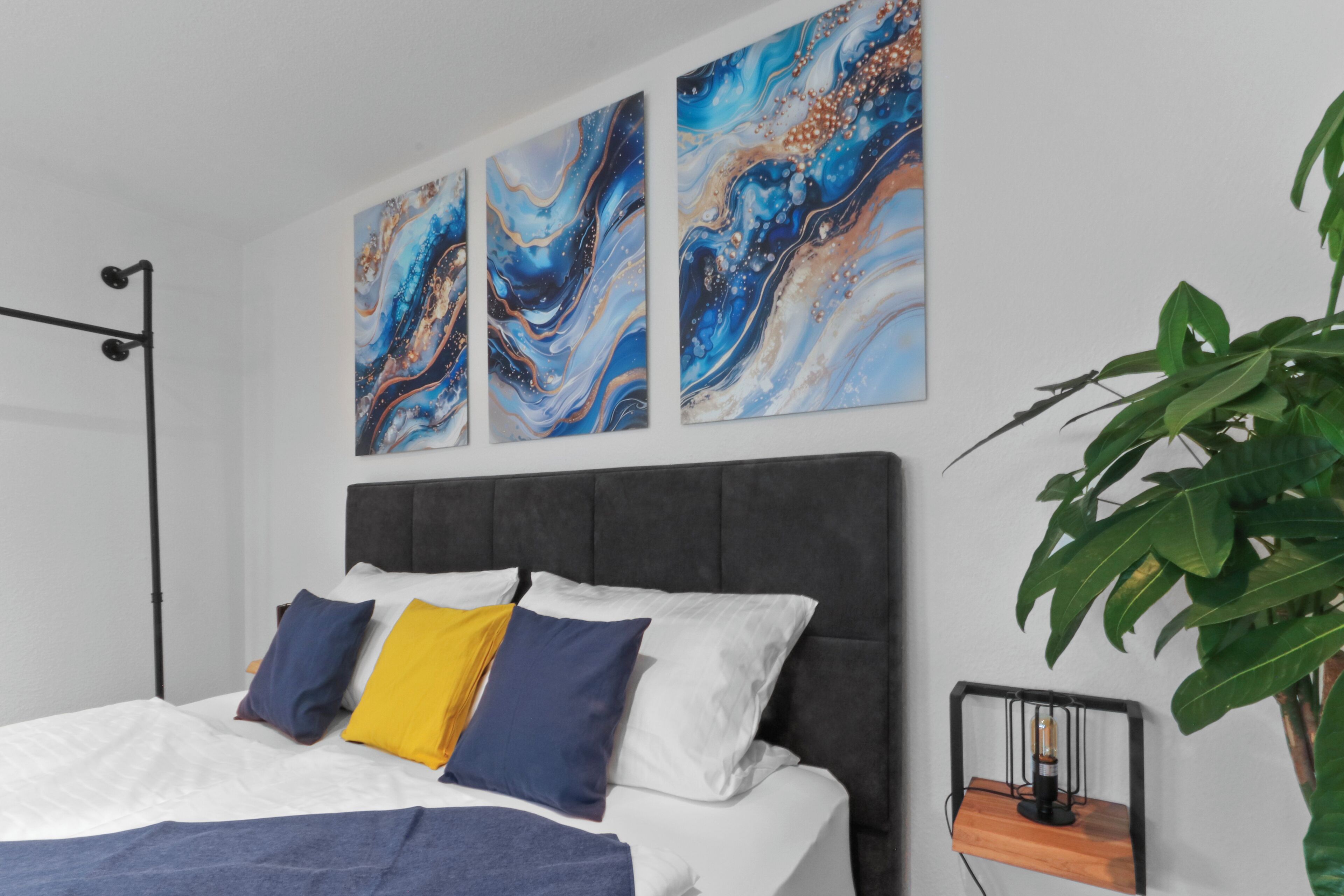 A modern bedroom with a bed, a nightstand, a floor lamp, and a large plant.