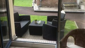 A balcony with wicker furniture, a grassy area, and a brick building in the background. - Charming 2 rooms old Lille, terrace, parking (Lille)