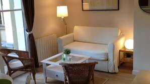 A modern living room with a white sofa, a glass coffee table, wicker chairs, and a floor lamp. - Charming 2 rooms old Lille, terrace, parking (Lille)