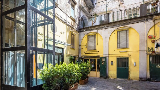 A courtyard with a glass building, stone paving, and yellow walls. - Residenza Diaz by Wonderful Italy (Naples)
