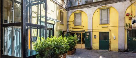 A courtyard with a glass building, stone paving, and yellow walls.