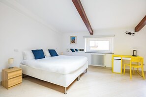 Ein Schlafzimmer mit Bett, Nachttisch, Schreibtisch, Stuhl, Fenster, Heizkörper und einem Bild an der Wand.
