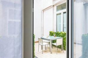 Une table en verre avec des chaises, une fenêtre et une haie à l’extérieur.