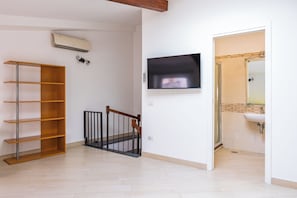 Ein Zimmer mit einem Holzbodenregal, einem an der Wand befestigten Fernseher und einem durch eine offene Tür einsehbaren Badezimmer.