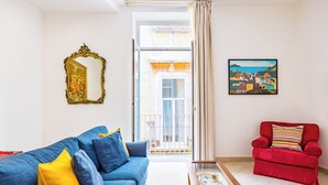 A living room with a blue sofa, a red armchair, a coffee table, a mirror, and a painting. - Residenza Diaz by Wonderful Italy (Naples)