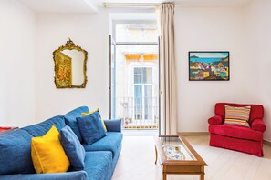 Un salon avec un canapé bleu, un fauteuil rouge, une table basse, un miroir et un tableau.
