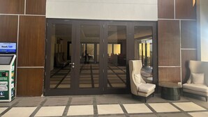A hotel entrance with a glass door, a reception desk, and a seating area with chairs and a table. - Chic 2-bedroom condo with WiFi, fitness room and Pool in vibrant Quezon City (Quezon City)
