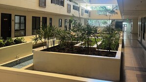 A multi-level atrium with a central garden area, balconies with railings, and framed artwork on the walls. - Chic 2-bedroom condo with WiFi, fitness room and Pool in vibrant Quezon City (Quezon City)