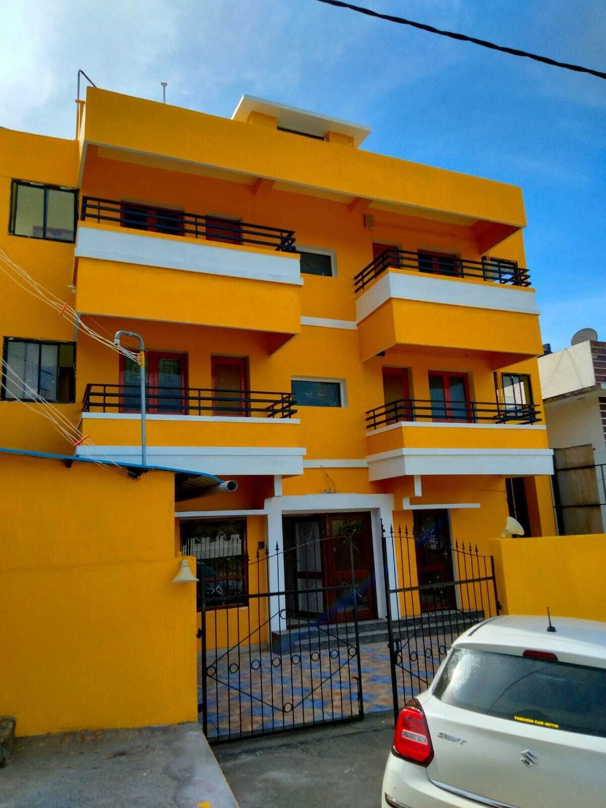 A multi-story yellow building with balconies, a gated entrance, and a parked car.