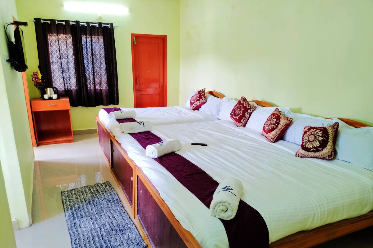 A hotel room with a large bed, a wooden headboard, a small table with a vase, and a red door.