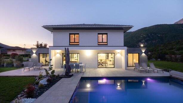Una casa moderna de dos pisos con piscina, mobiliario de exterior y un jardín bien cuidado.