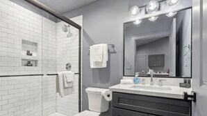 Un baño moderno con cabina de ducha de vidrio, un inodoro blanco, un tocador con espejo y un lavabo.